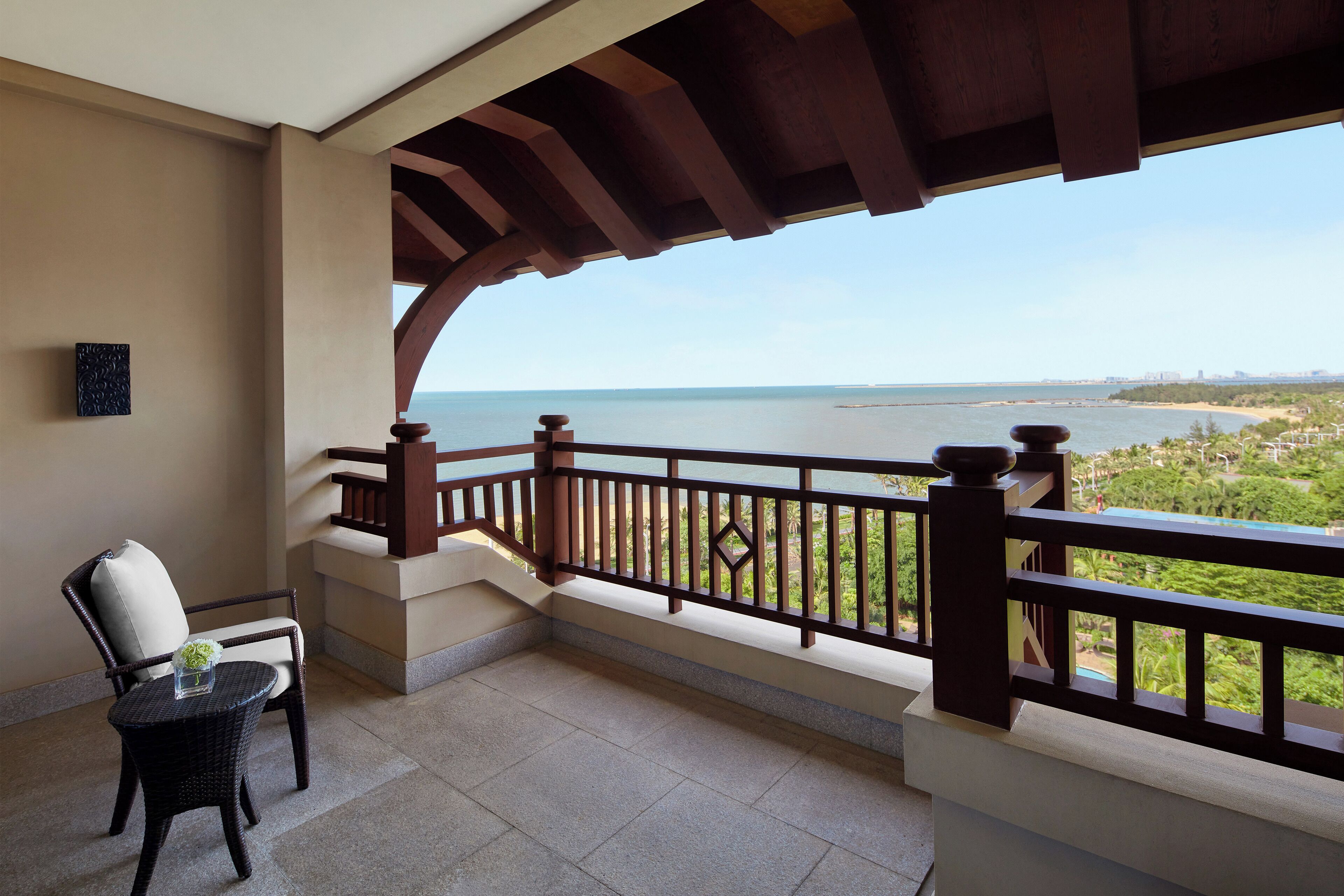 Un balcon avec vue sur la mer, une chaise en osier et une petite table sur laquelle est posé un vase.