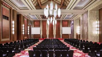 Un salón de conferencias con filas de sillas, una alfombra roja y una pantalla grande al frente.