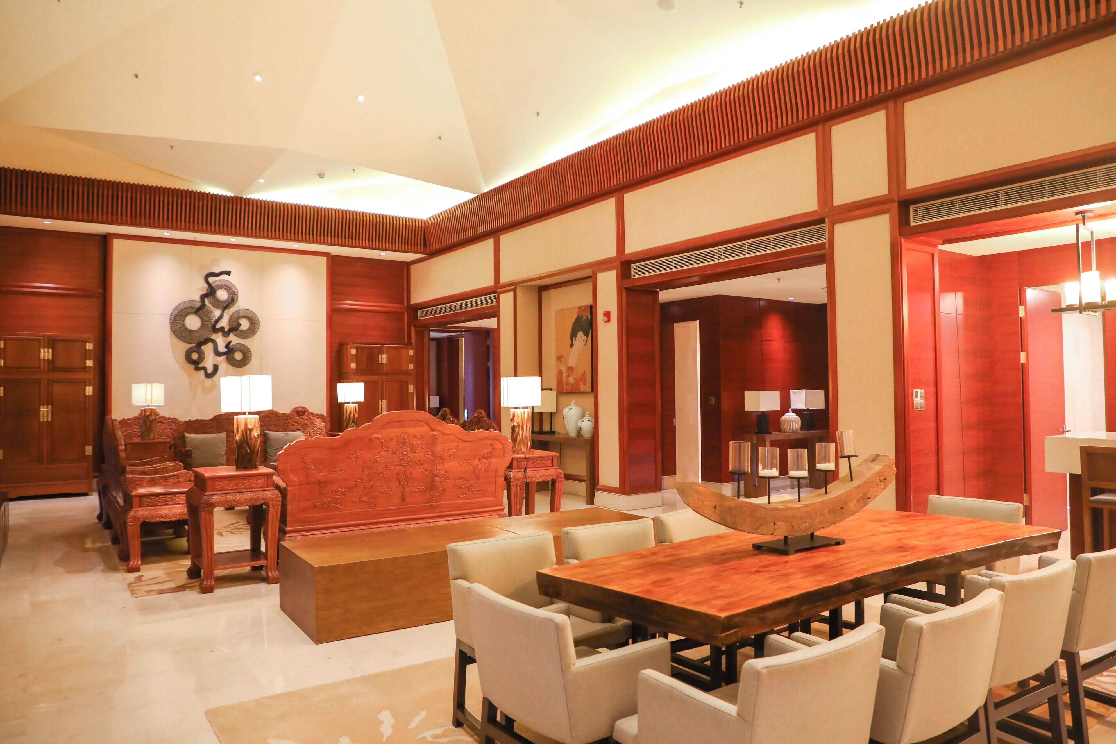 Eine großzügige Hotelhalle mit einem großen Holzbüro für die Rezeption, mehreren Sitzbereichen und Wanddekoration im traditionellen asiatischen Stil.