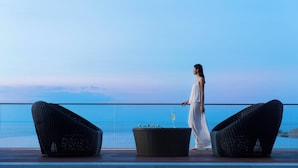 A person walking on a balcony with a view of the sea, two wicker chairs, and a table with a drink. - Haikou Marriott Hotel (Haikou)
