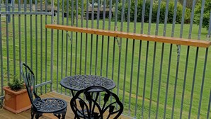 Una terraza de madera con dos mesas y sillas de metal, una planta en maceta y una valla metálica.