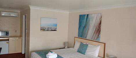 A hotel room with a bed, a desk, a microwave, and a small kitchenette.