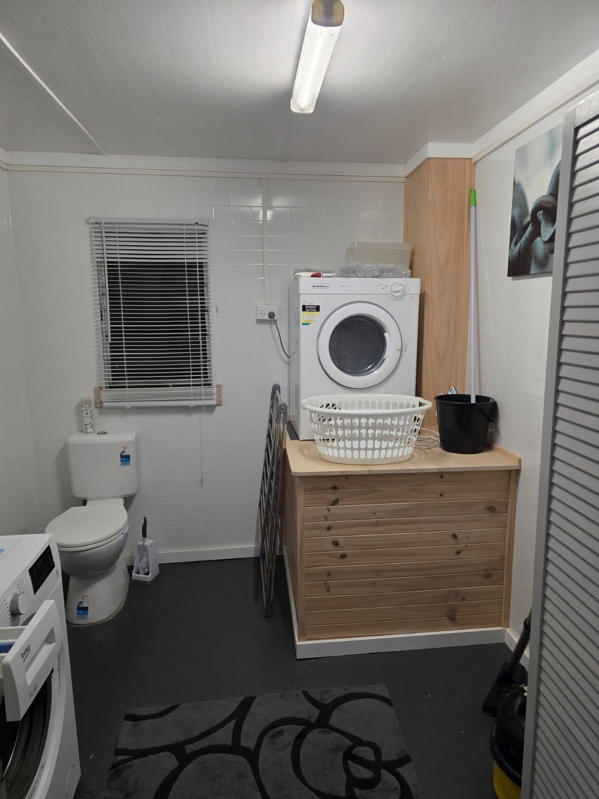 Een kleine wasruimte met een wasmachine, een droogrek en een klein houten aanrecht.