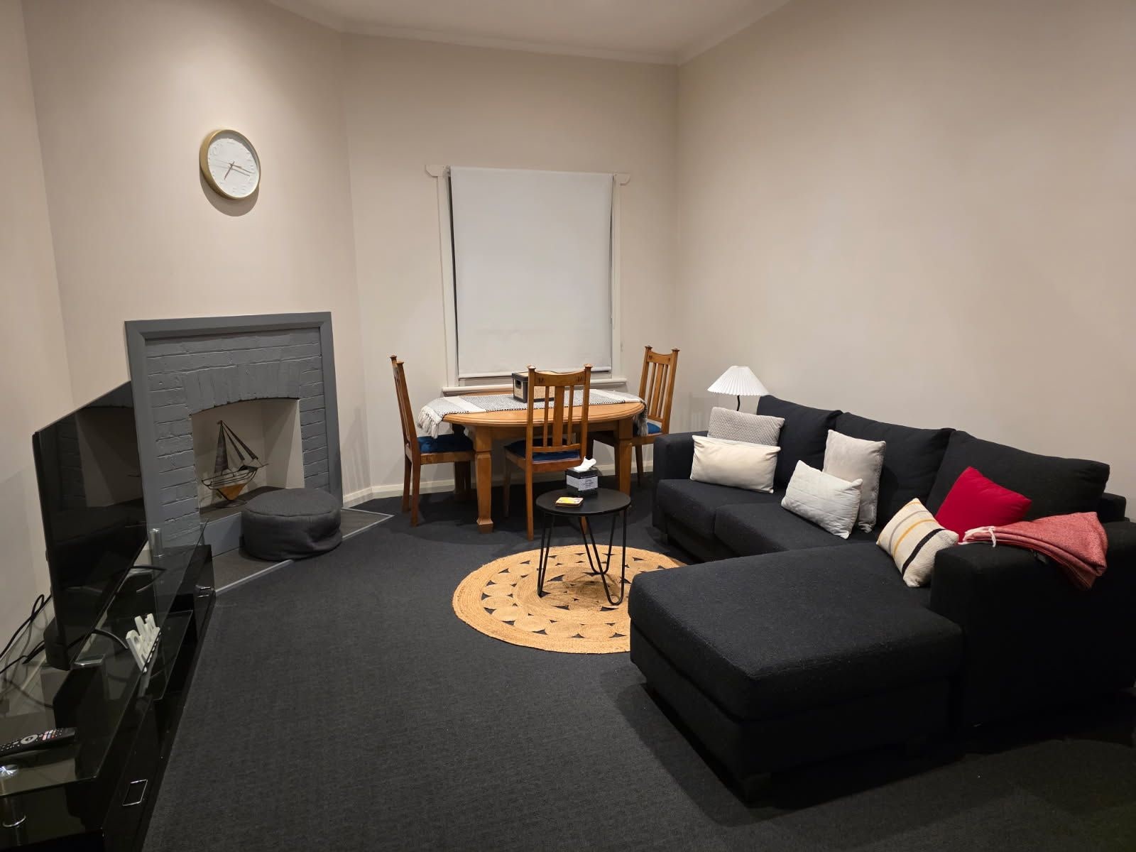 A living room with a fireplace, a dining table with chairs, a black sofa, and a television.