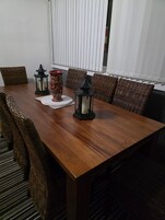 Una mesa de comedor con sillas de mimbre, dos faroles negros y un florero rojo.