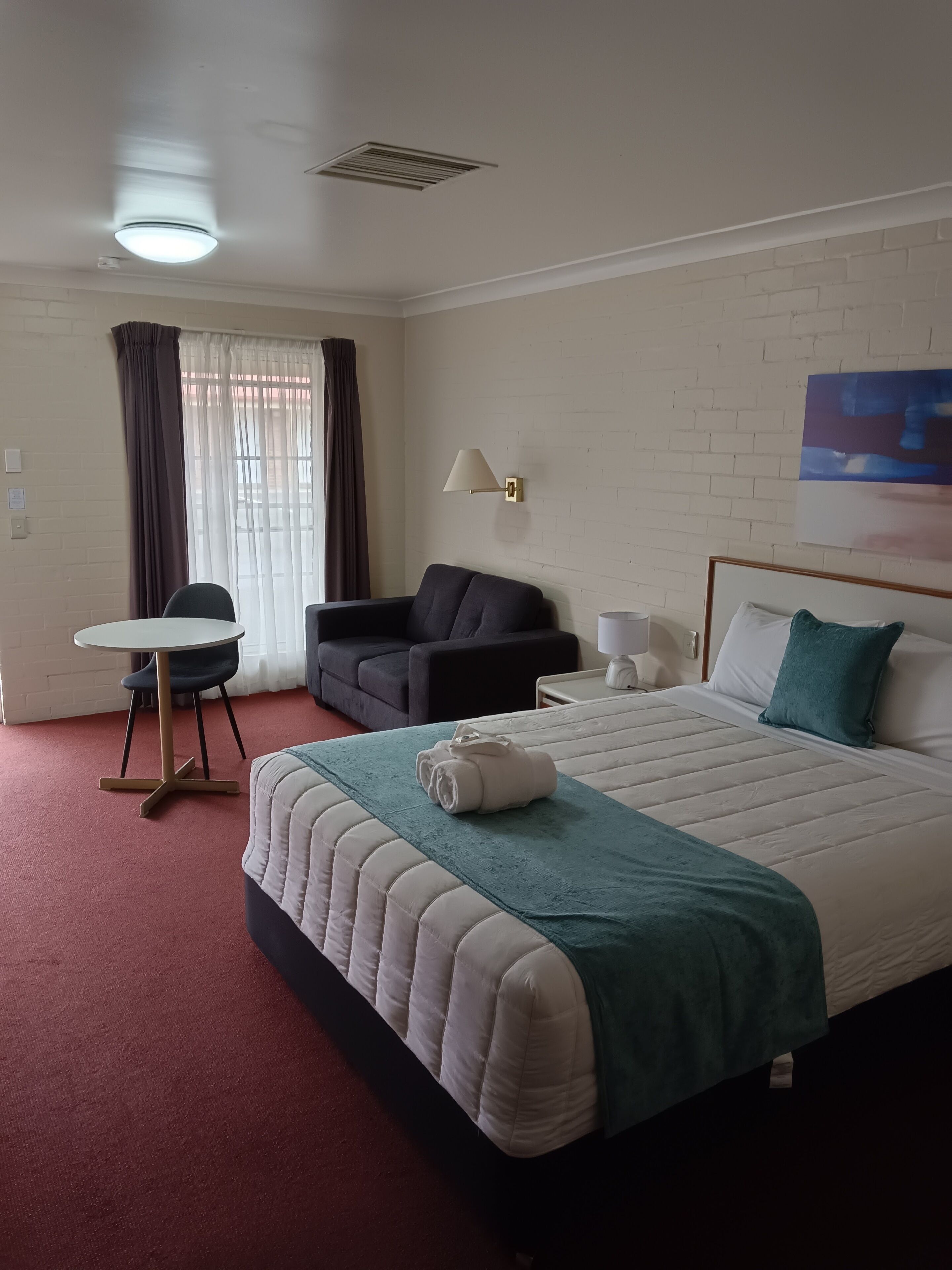 Una habitación de hotel con cama, escritorio, sillón, sofá y un cuadro en la pared.