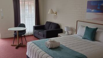 Una habitación de hotel con cama, escritorio, sillón, sofá y un cuadro en la pared.