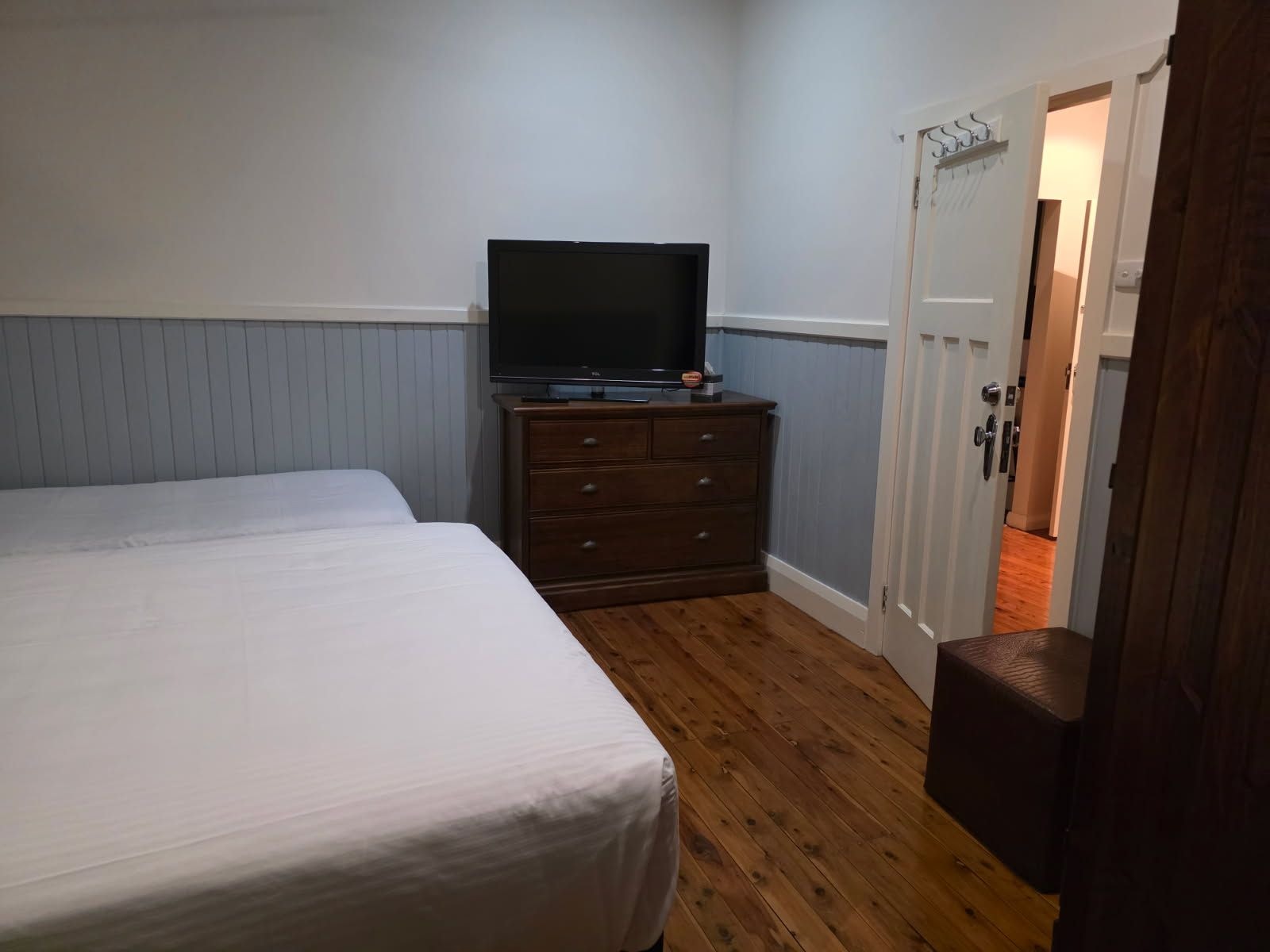 Un dormitorio con cama, cómoda, televisor y puerta que da a otra habitación.