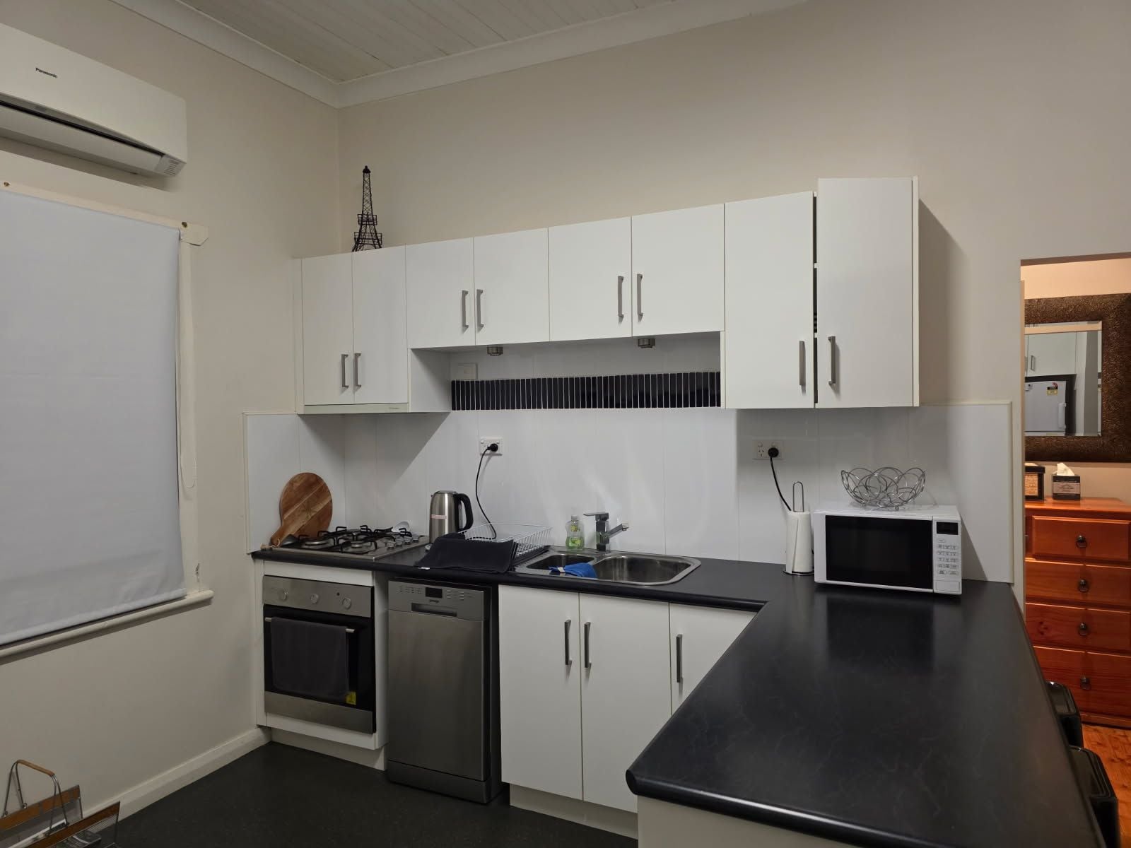 A compact kitchen with white cabinets, a black countertop, a stainless steel dishwasher, a gas stove, and a microwave.
