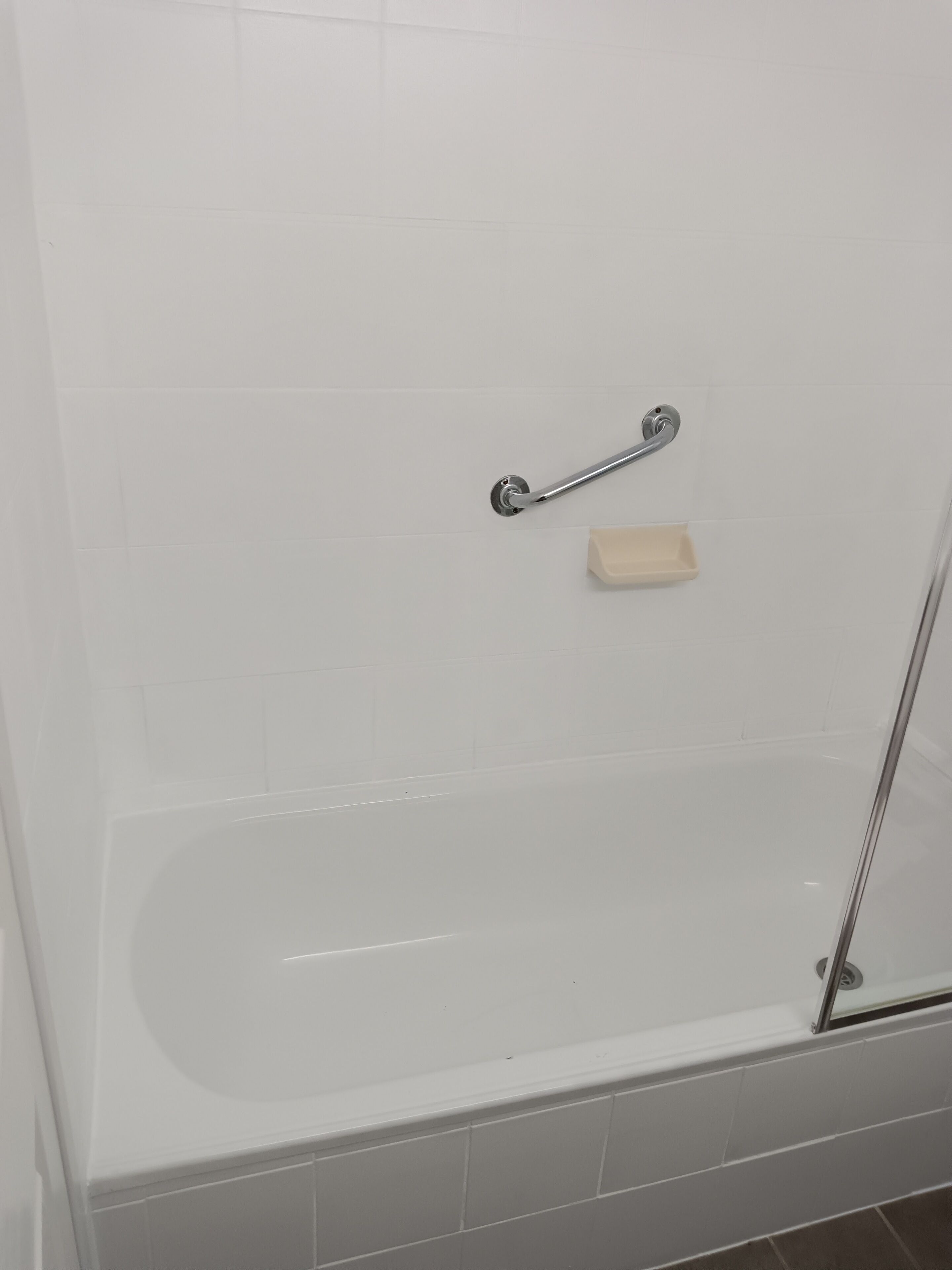 Una bañera blanca con puerta de cristal, un cabezal de ducha manual y un jabonera.