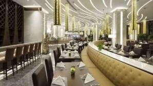 A modern restaurant interior with a curved seating area, high ceiling with linear light fixtures, and a bar counter. - Ramada Plaza Xian South (Xi'an)