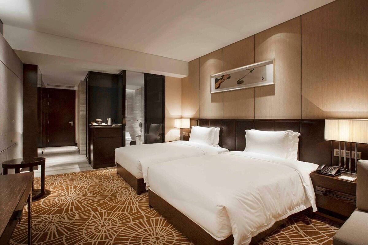 Une chambre d’hôtel avec deux lits, un bureau, une chaise, un téléphone et un tableau au mur.