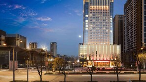 A high-rise hotel with a prominent illuminated sign, surrounded by modern buildings and a well-lit urban street. - Ramada Plaza Xian South (Xi'an)