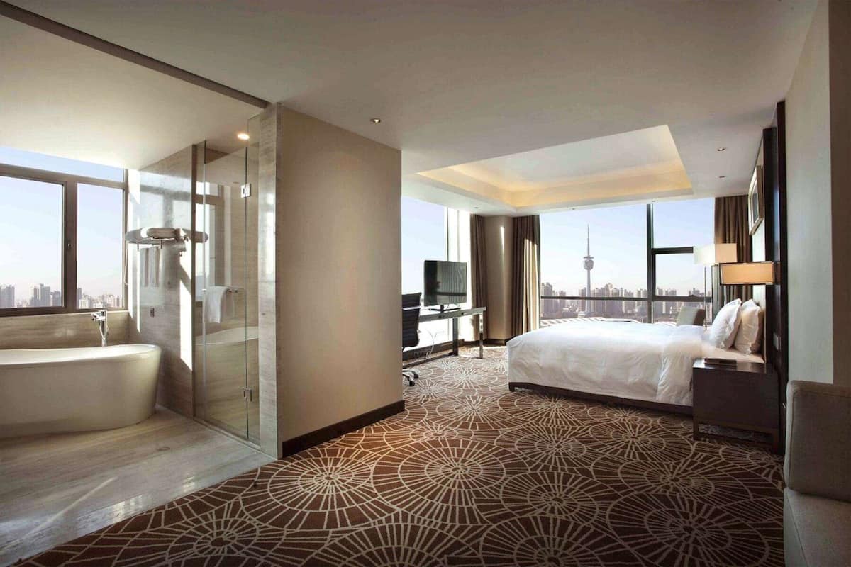 Une chambre d’hôtel avec un grand lit, une salle de bain séparée avec une baignoire, un bureau avec une télévision et une vue sur le panorama urbain.