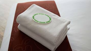 Une serviette blanche, soigneusement pliée, ornée d’un logo circulaire vert, posée sur un coussin marron.
