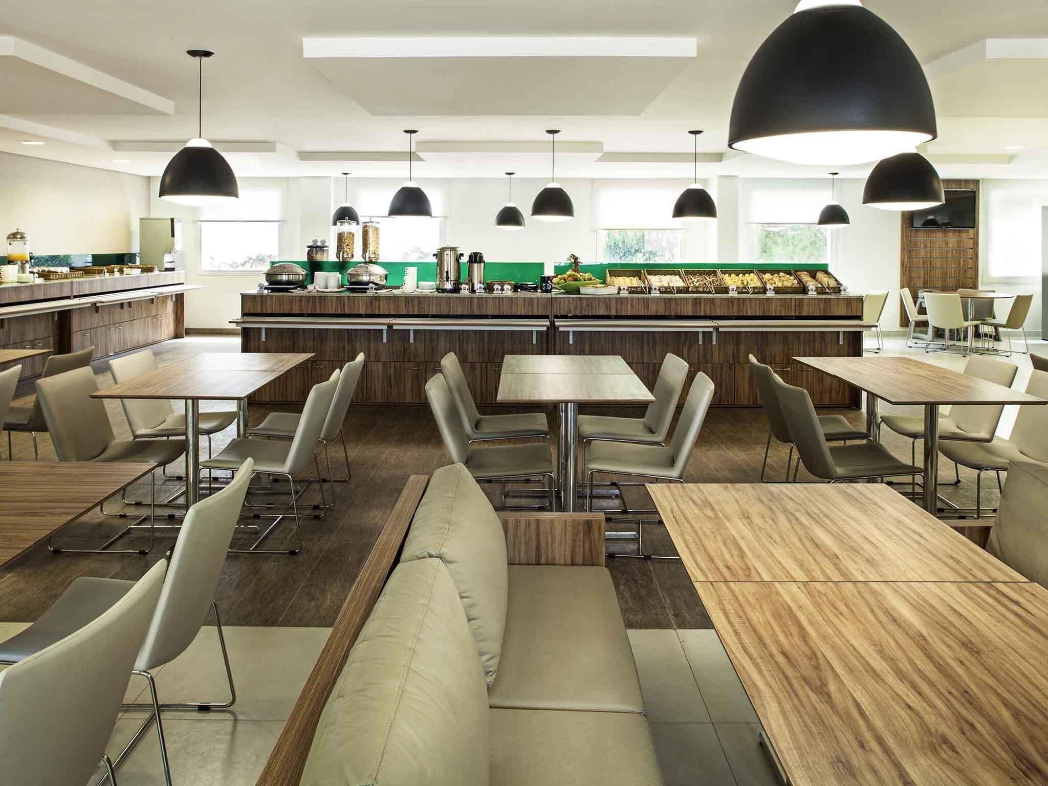 Een modern restaurant met hoge tafels en zitjes, hangende verlichting en een centrale balie met etalages.