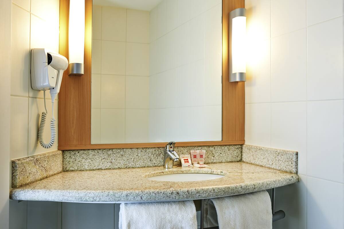 A bathroom with a granite countertop sink, a mirror, a hair dryer, and a towel rack.