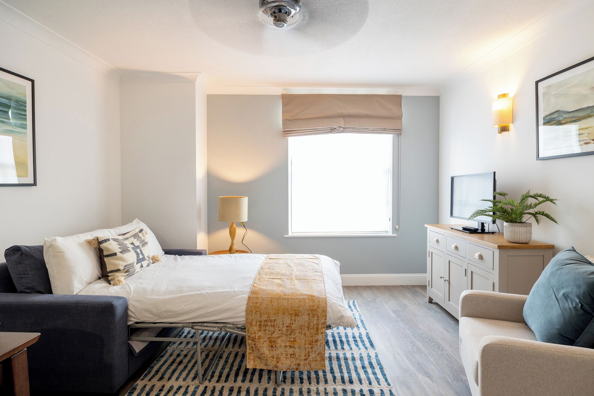 Een slaapkamer met een bed, nachtkastje, lamp, kaptafel en een raam.