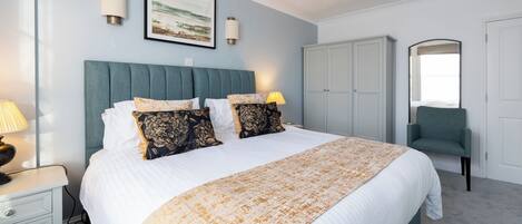 A bedroom with a bed, bedside lamps, a headboard, a wardrobe, and a chair.