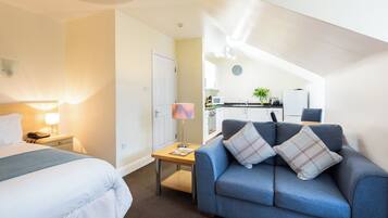 Habitación de hotel con una cama, un escritorio, un sofá y una kitchenette al fondo.