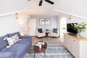 A modern living room with a sofa, armchair, coffee table, TV, and a plant. - SACO Jersey Merlin House (St. Helier)