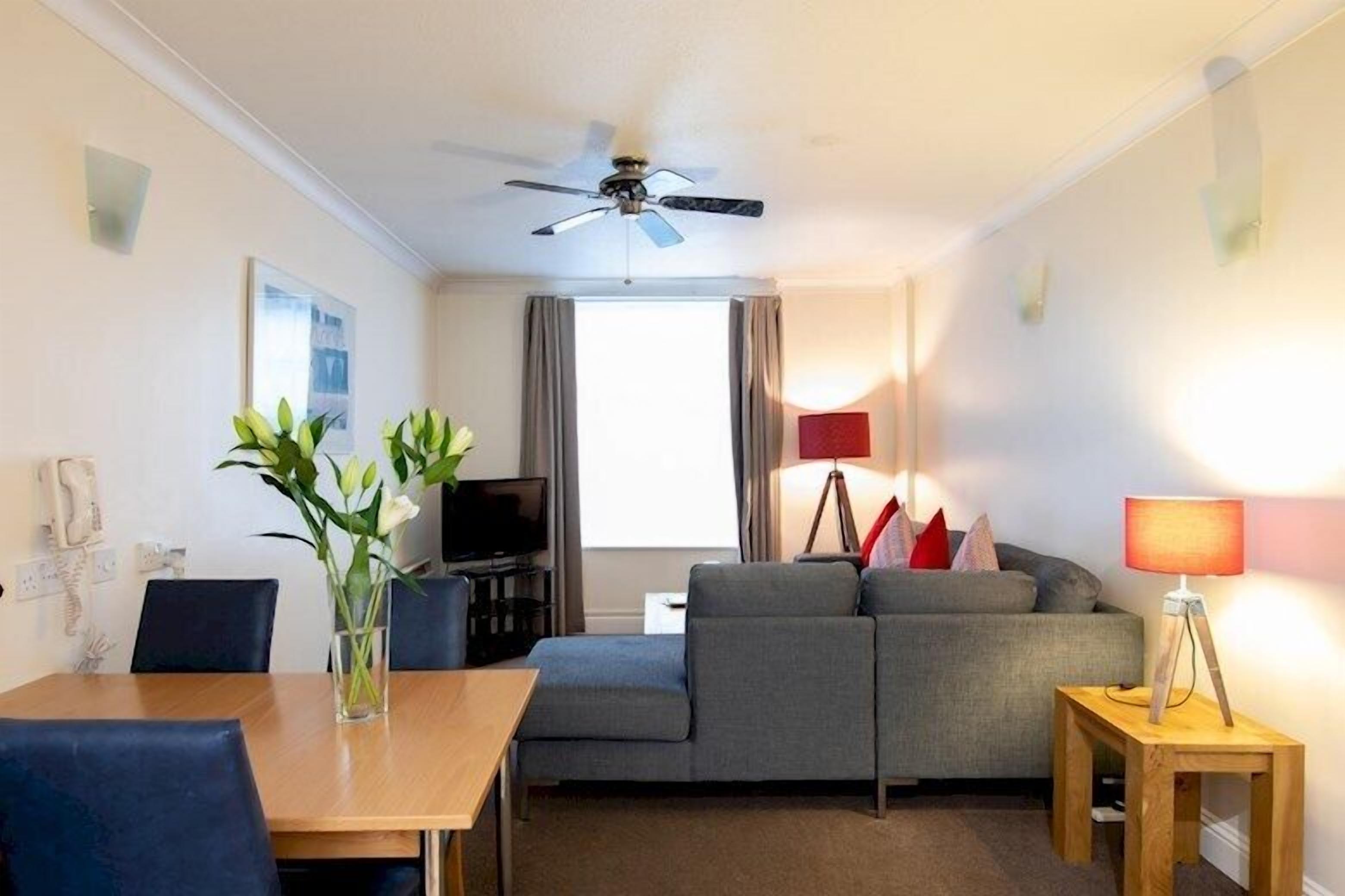 A hotel room with a sofa, a TV, a dining table, and a ceiling fan.