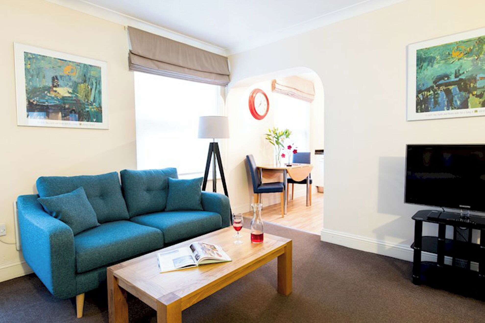 A living room with a sofa, coffee table, and a television. There is a dining area with a table and chairs.
