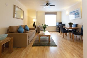 A living room with a sofa, coffee table, and a dining area with chairs and a table. - SACO Jersey Merlin House (St. Helier)