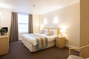 A hotel room with a bed, bedside table, lamp, and a view of the outdoors. - SACO Jersey Merlin House (St. Helier)