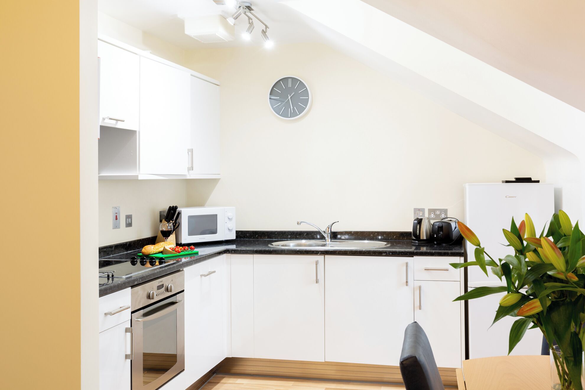 A modern kitchen with white cabinets, a microwave, a sink, and a clock on the wall.