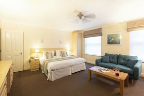 A hotel room with a bed, a sofa, a coffee table, a desk, and a window. - SACO Jersey Merlin House (St. Helier)