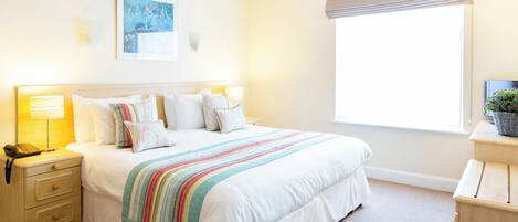 A hotel room with a bed, bedside lamps, a nightstand, a window with a view, and a painting on the wall.