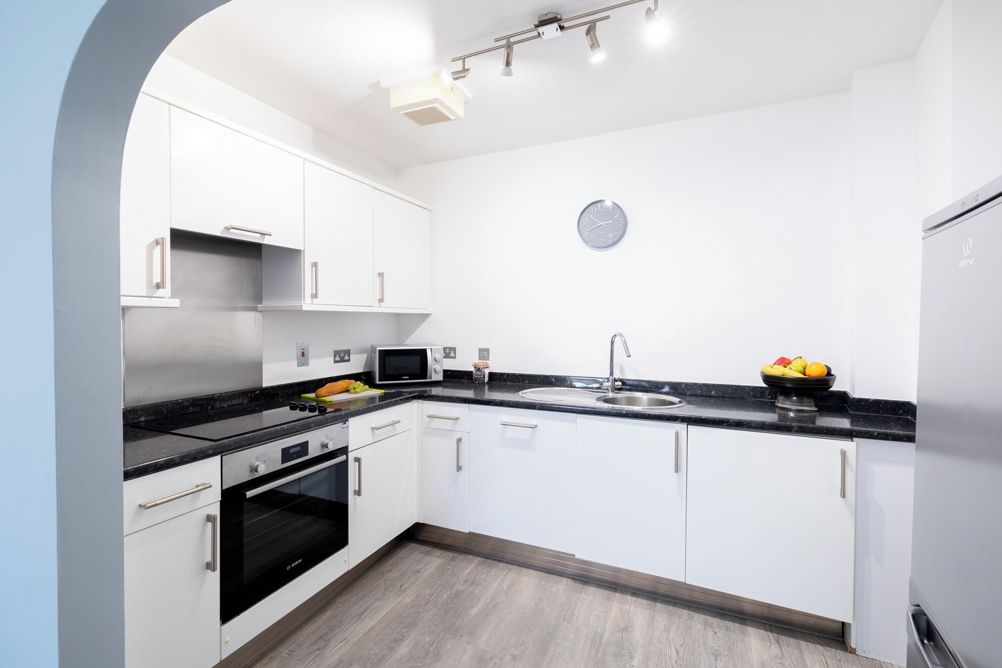 A modern kitchen with white cabinets, a black countertop, a built-in oven, a microwave, and a sink.