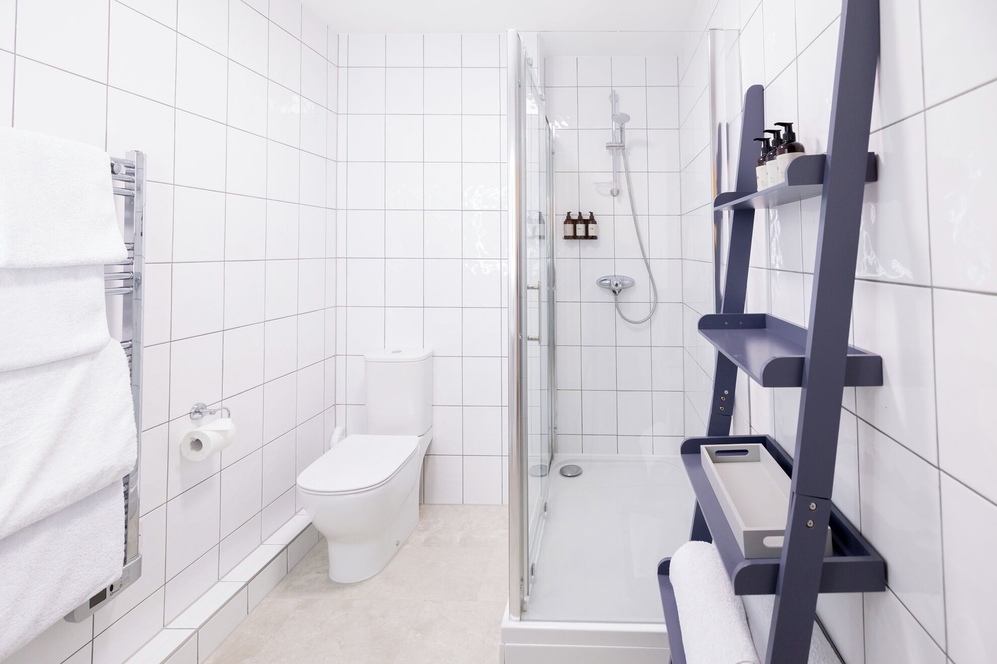 A modern bathroom with white tiles, a toilet, a shower enclosure, and built-in shelves.