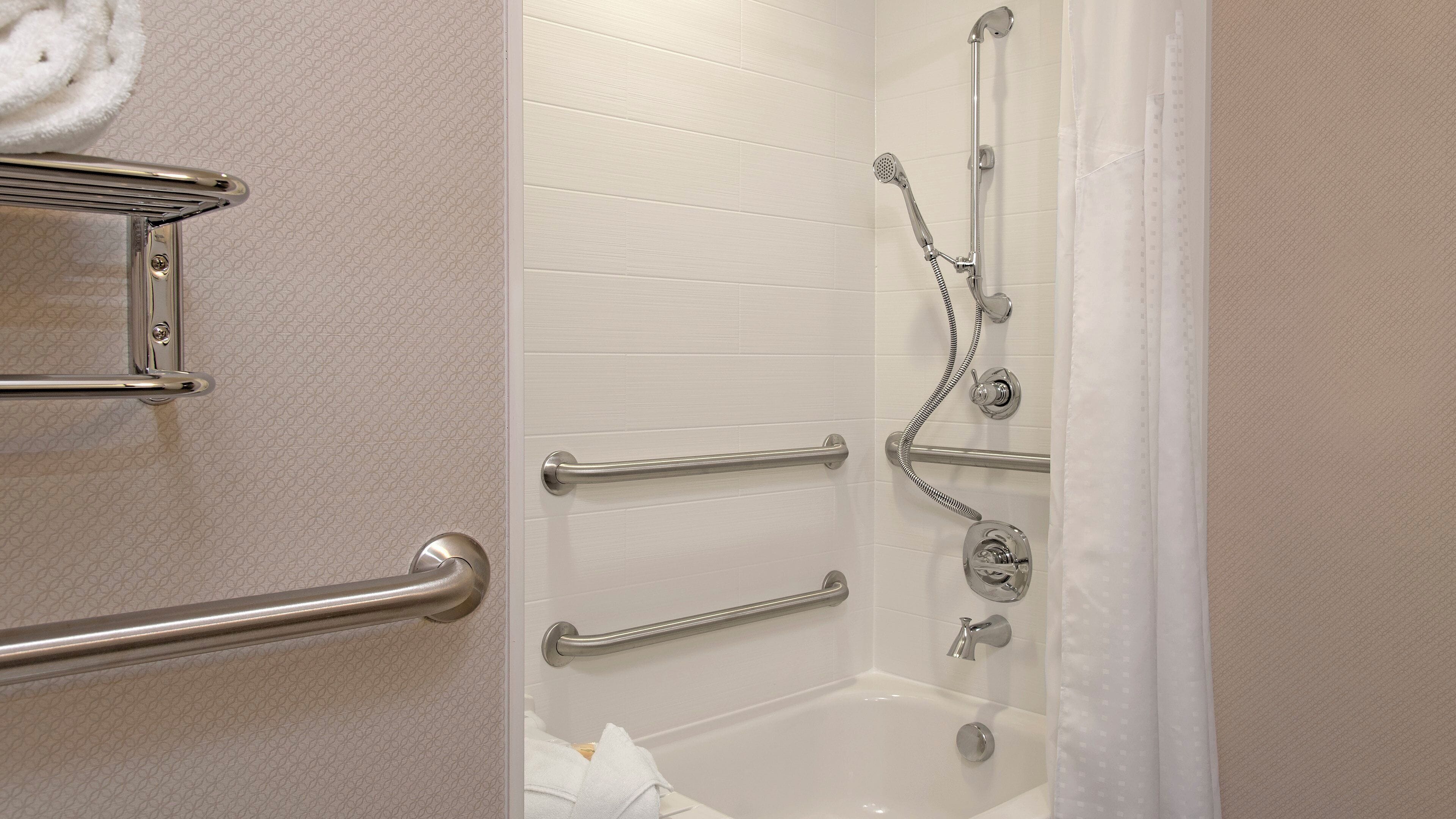 Ein Badezimmer mit einer Badewanne, einer Dusche inklusive Duschbrause und Haltegriffen.