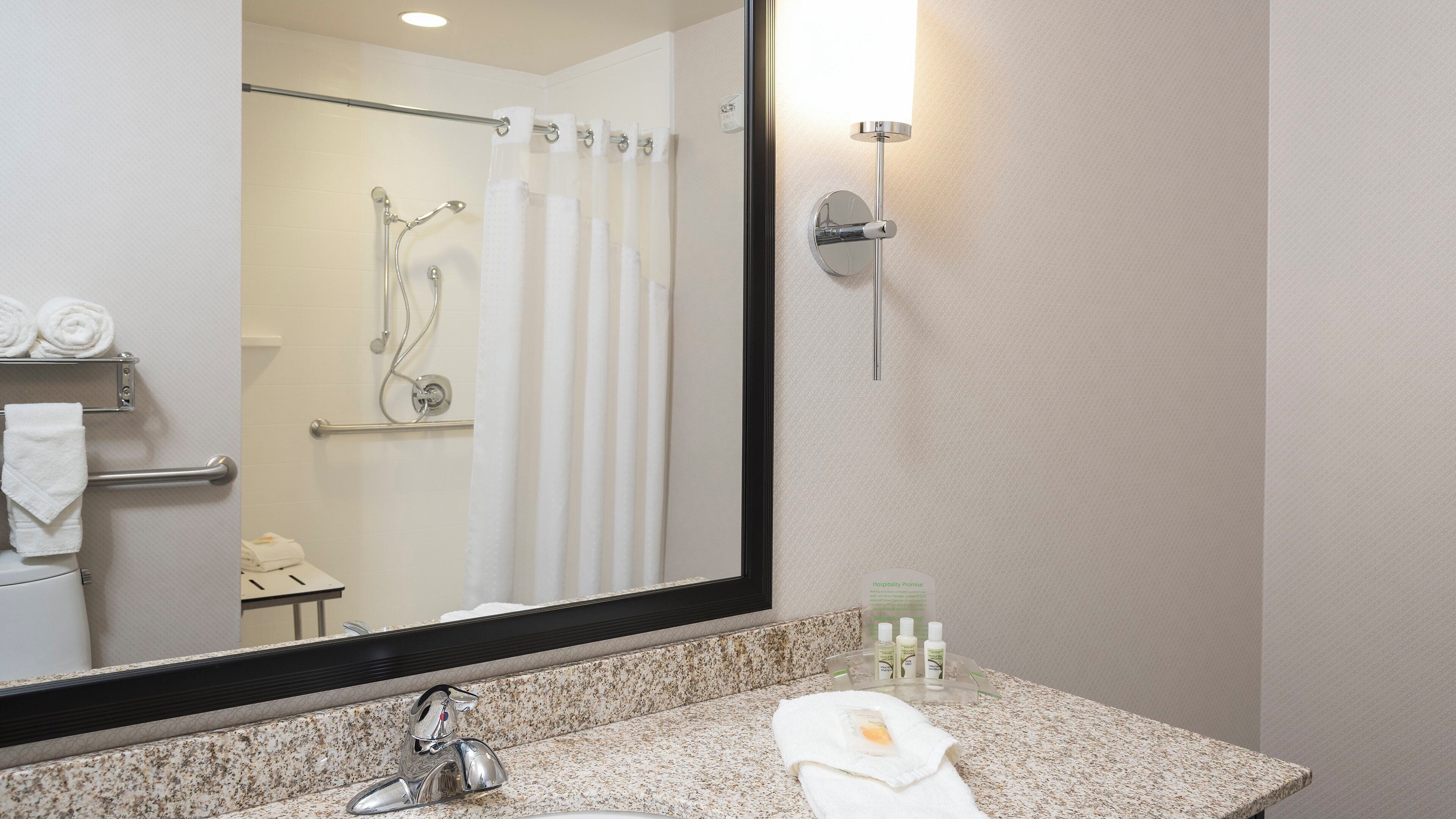 A bathroom with a sink, mirror, shower, towel rack, and toiletries.