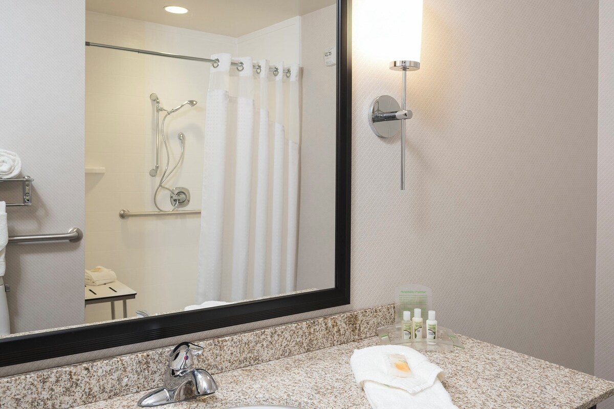 A bathroom with a sink, mirror, shower, towel rack, and toiletries.