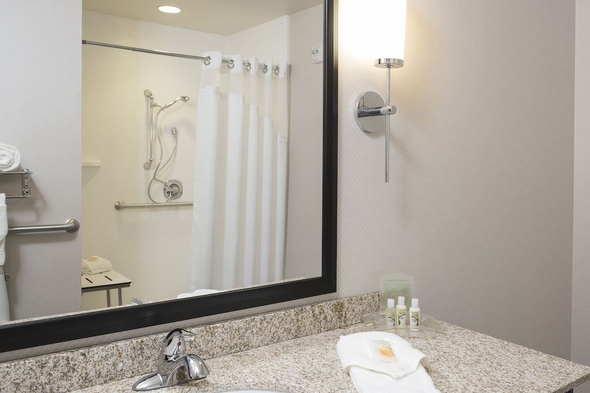 A bathroom with a granite countertop, a sink, a mirror, and a shower area with a curtain.
