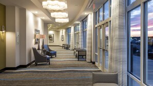 A hotel lobby with a striped carpet, seating area with chairs, a table, and large windows with curtains. - Holiday Inn Indianapolis Airport by IHG (Indianapolis)