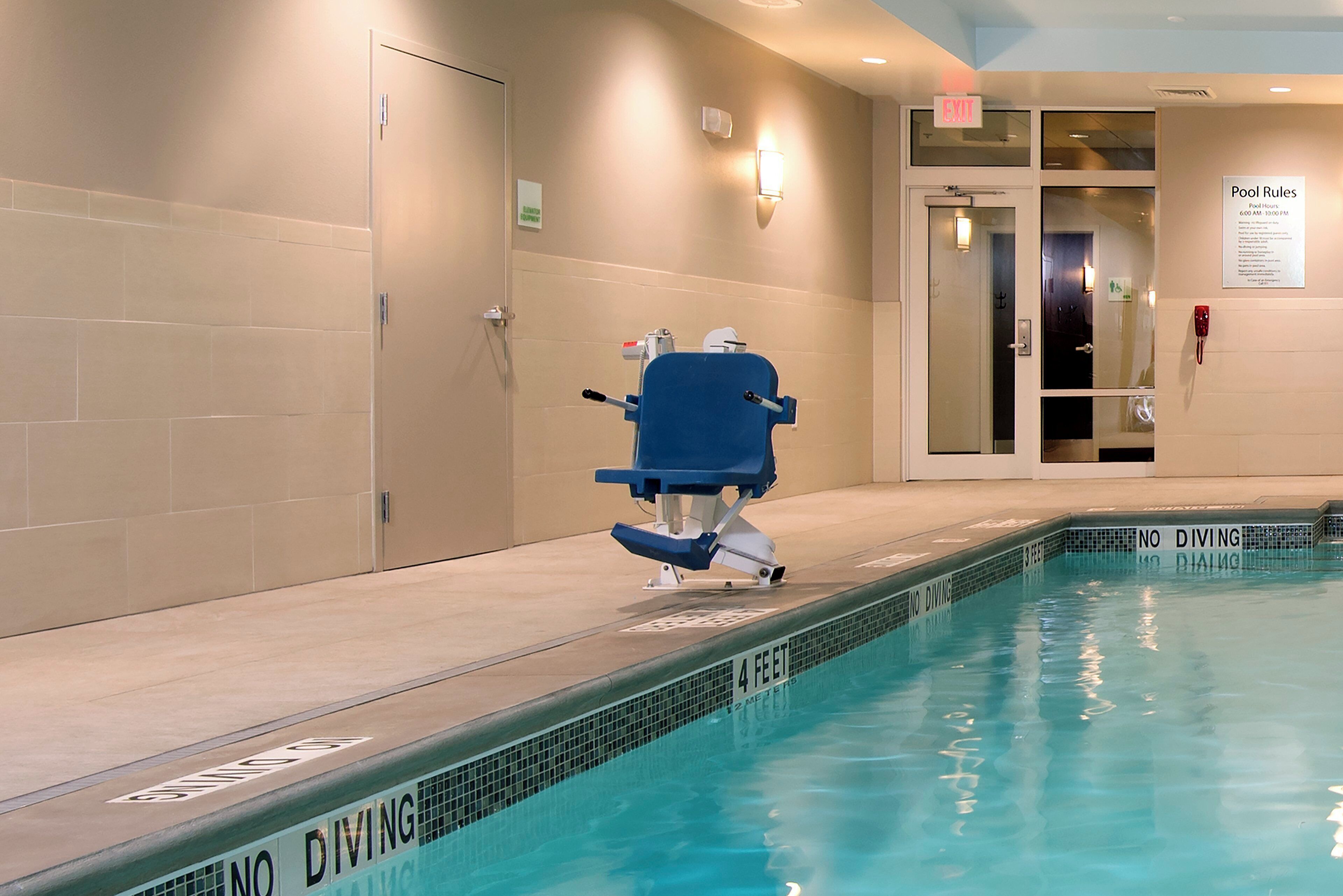 A pool area with a diving board, pool rules sign, and a door leading to another room.