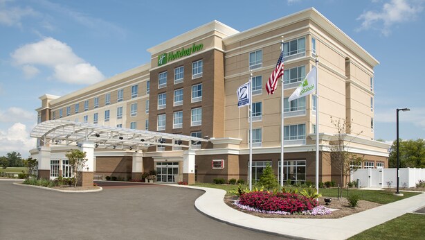 A Holiday Inn hotel with a covered entrance, a parking lot, and a landscaped area with flowers. - Holiday Inn Indianapolis Airport by IHG (Indianapolis)