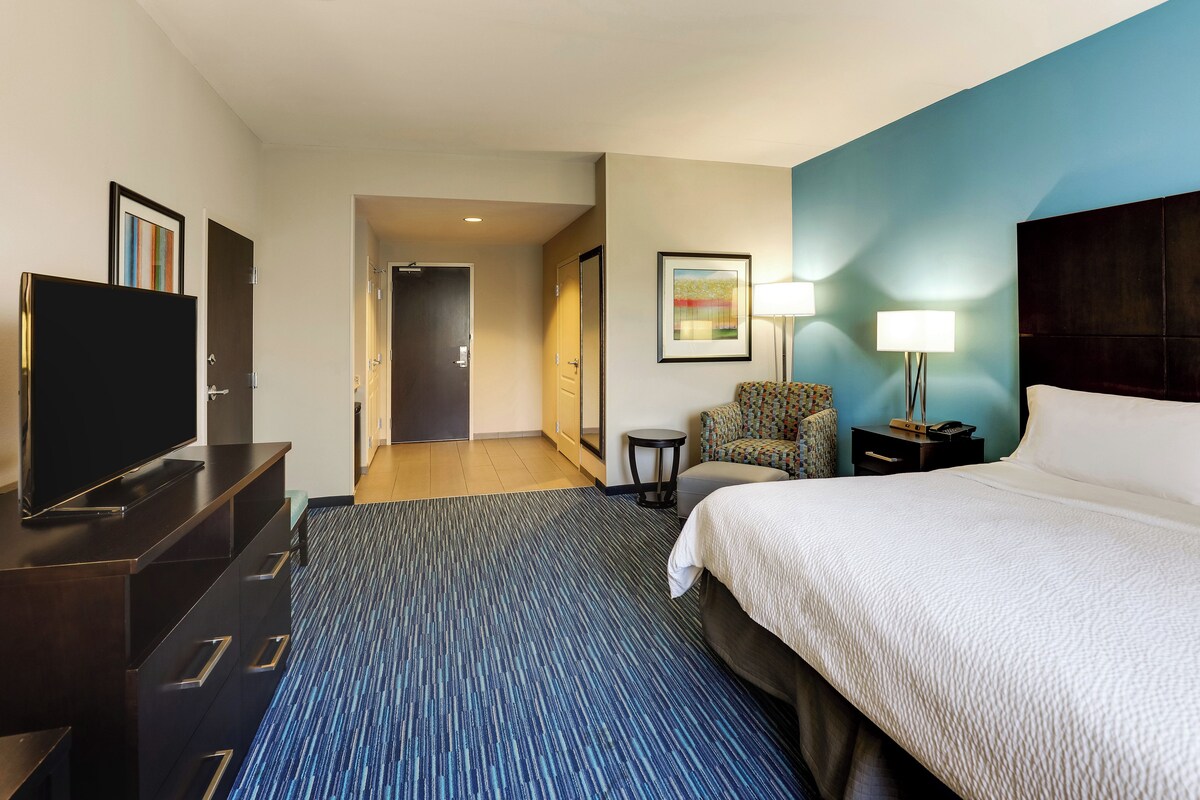 A hotel room with a bed, a TV, a desk, a chair, and a lamp.