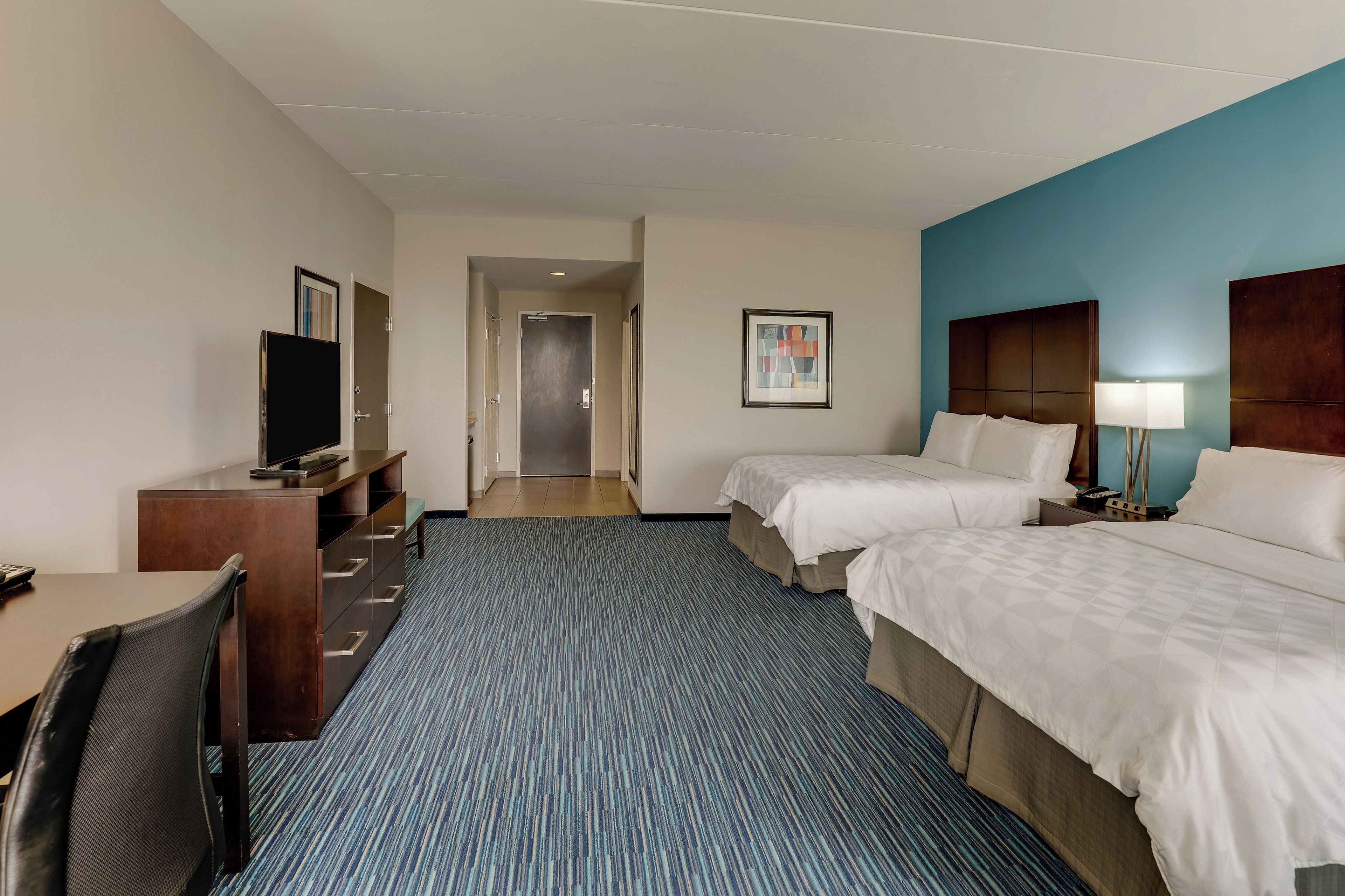 Une chambre d’hôtel avec deux lits, un bureau, une chaise, une télévision et une porte de salle de bain.