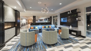 A modern hotel lobby with a seating area, a fireplace, and a television. - Holiday Inn Indianapolis Airport by IHG (Indianapolis)