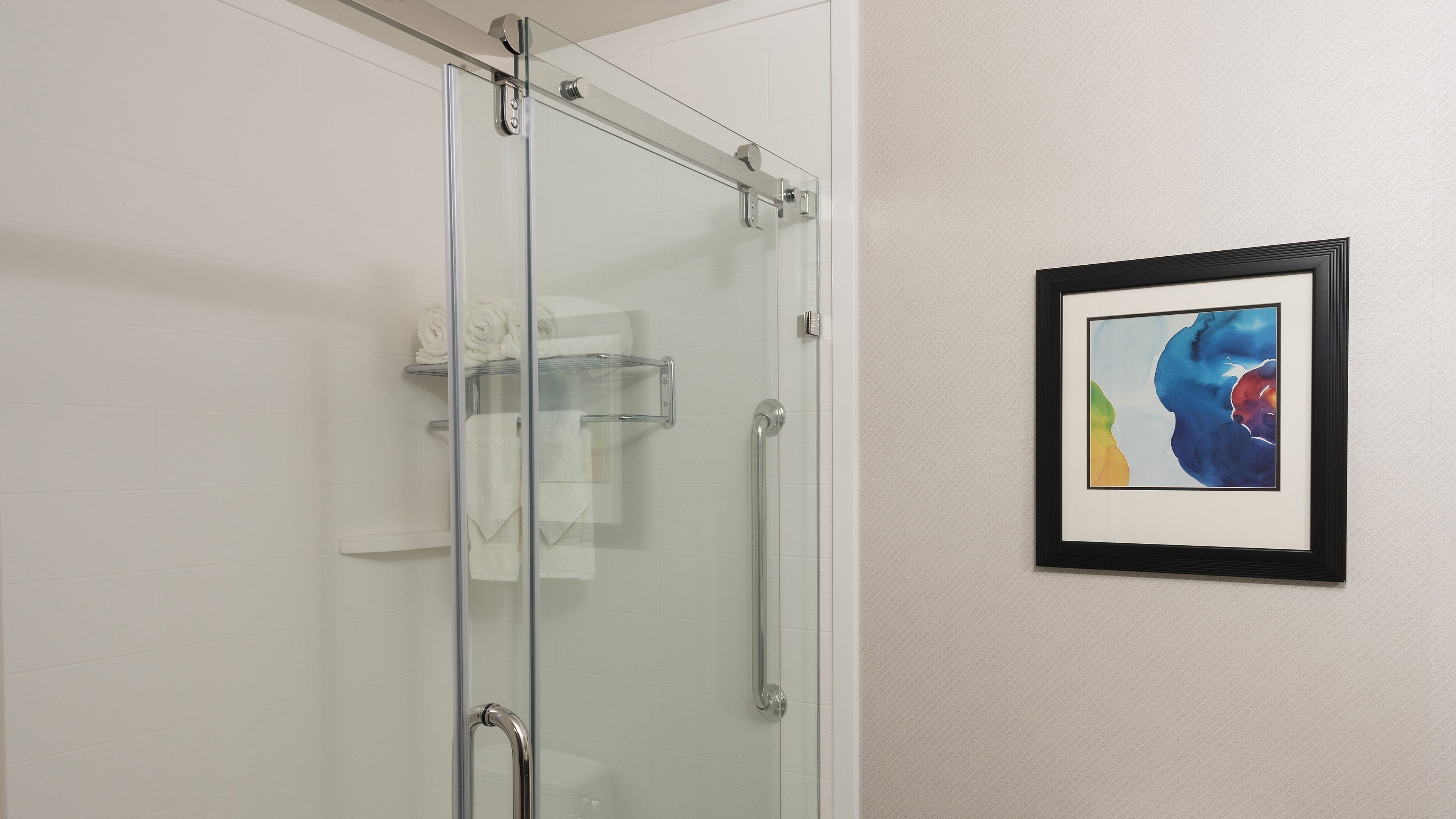 A glass shower enclosure with a towel rack and a framed abstract painting on the wall.