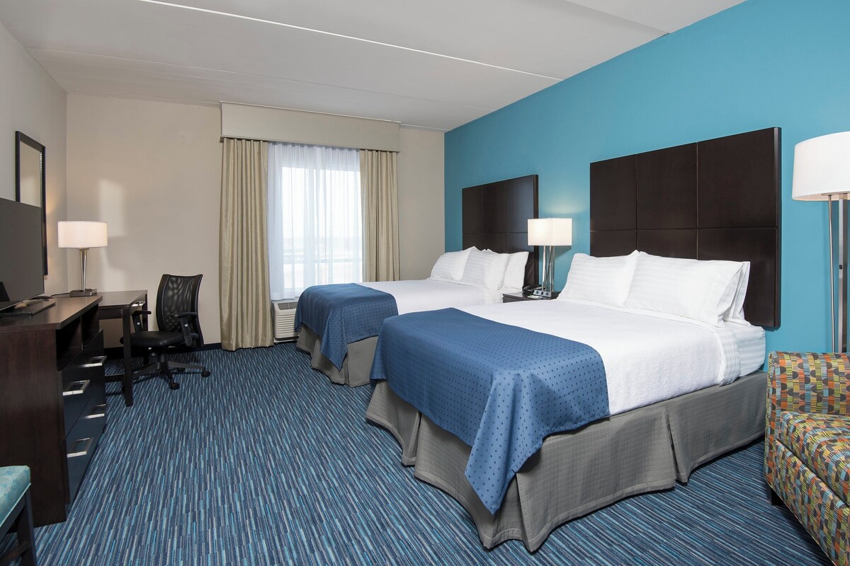 A hotel room with two beds, a desk, a chair, a TV, and a patterned sofa.