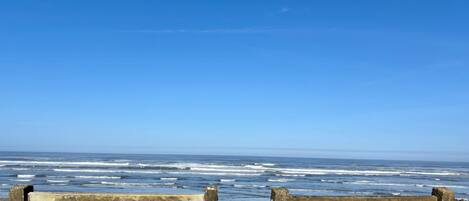 Two wooden benches facing the ocean with waves crashing onto the shore under a clear blue sky.