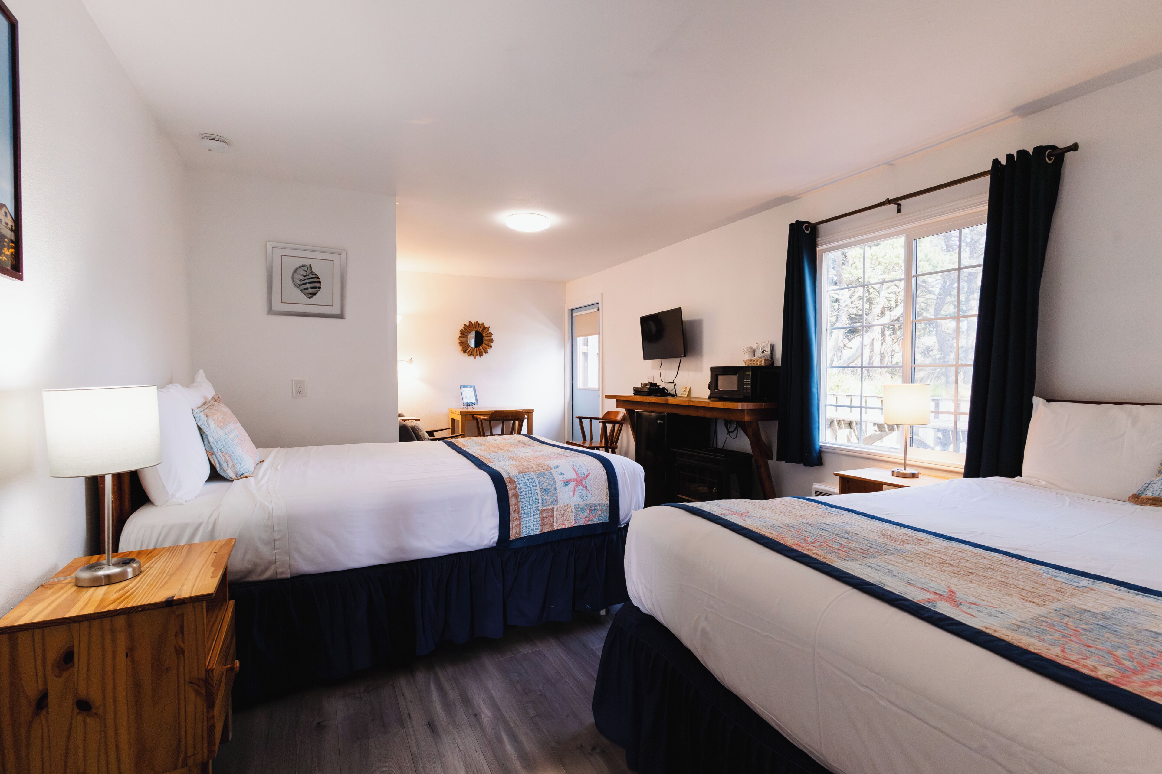 A hotel room with two beds, a desk, a chair, a TV, and a window with curtains.