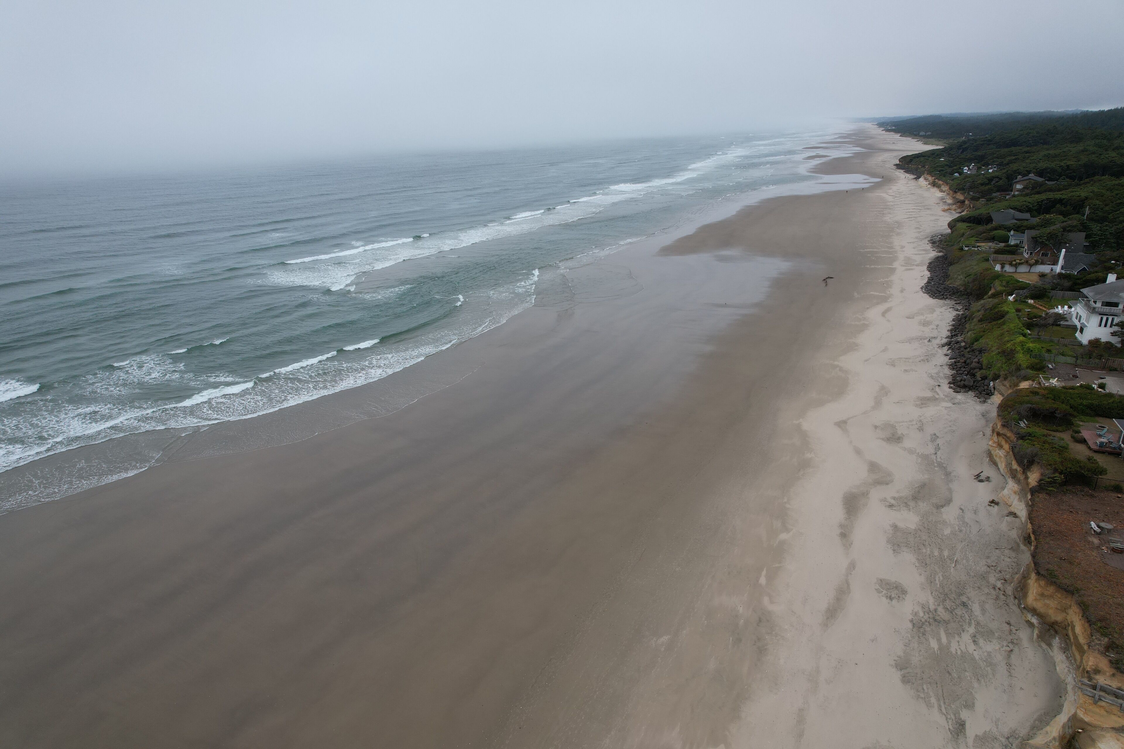 Une plage côtière avec un rivage sablonneux, quelques maisons et une falaise.