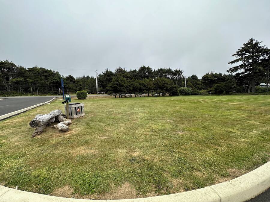 A grassy area with a curb, a blue sign, and a wooden structure.